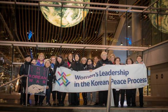 A group of about 20 Korean and Canadian women, with a banner saying Women's Leadership in the Korean Peace Process.